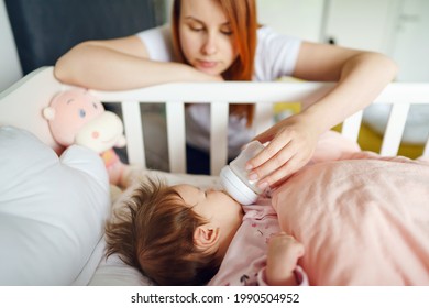 Front View Of Caucasian Woman Mother Taking Care Of His Newborn Baby Child Two Months Old Bottle Feeding With Breast Or Formula Milk While Child Is Lying In Cradle At Home Selective Focus Copy Space