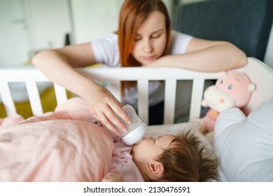 Front view of caucasian woman mother taking care of his newborn baby child two months old bottle feeding with breast or formula milk while child is lying in cradle at home selective focus copy space