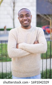 Front view of cheerful guy standing and looking at camera. Smiling African American man with crossed arms posing outdoors. Citizen concept