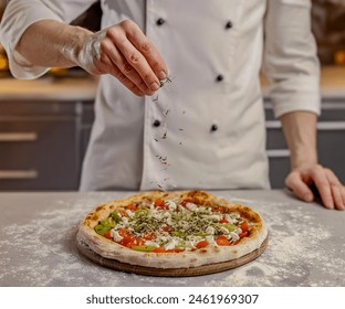 Front view of a chef sprinkling herbs onto a baked pizza. - Powered by Shutterstock