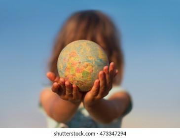 Front View Of A Child Hand Holding A Damaged Toy Globe In Front Of His Face