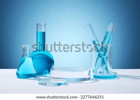 Front view of circle transparent podium and laboratory glassware filled with blue water. Empty area to display product. Concept of chemical, scientific experiment
