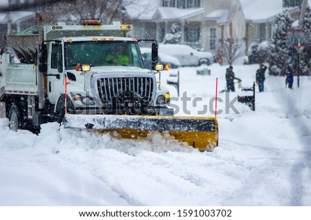 Front view of city services snow plow truck with yellow push blade clearing covered roads after heavy winter snow fall and passing by children bundled in warm clothes playing while flakes still fall. Foto d'archivio © 