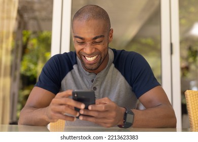 Front view close up of an African American man with gray t shirt sitting on the patio, using his mobile phone and smiling  - Powered by Shutterstock