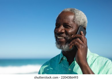 Front view close up of a senior African American man standing on the beach with blue sky in the background, smiling and talking on the phone - Powered by Shutterstock