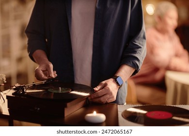 Front view close up of unrecognizable man setting up vinyl record player and enjoying retro music with ambiance copy space