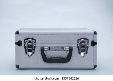 Front view of a closed aluminum case in silver with black handle and two locks, against a gray background