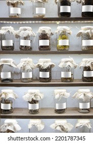 Front View Closeup Of Hand Made Glass Jar Recipients Containing Dried Spices And Ingredient Condiments With Empty White Labels And White Fabric Enclosures Stacked On Pantry Shelves