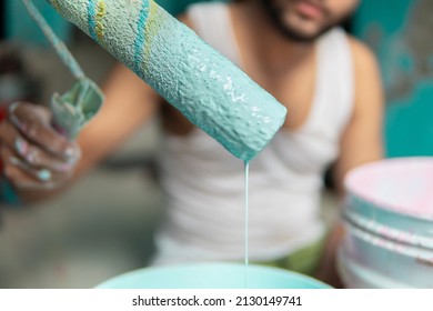 Front View Close-up Image Of Painter Holding Paint Roller And Mixing Wall Paint The Bucket.  