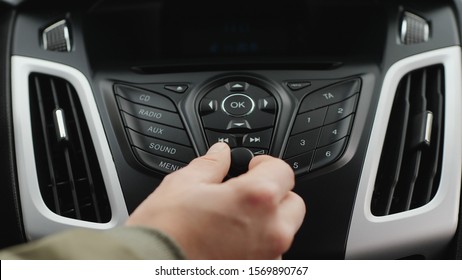 Front View Close-up Of Male Hand Adjust The Volume Or The Tuning Of The Car Radio. The Driver Turns The Switch On The Dashboard Of The Car