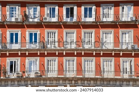 Front view of a colorful orange facade with white doors or jalousies. Balconies with white shutters or blinds on an orange exterior. Latin or Spanish architecture in Plaza Mayor - Madrid, Spain