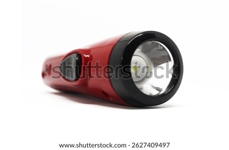 Front view of a compact, red flashlight lying on a white surface. The lens and the control switch are clearly visible in the well-lit setting.