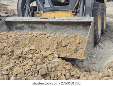 Front view of a compact wheel loader scooping gravel and soil into the bucket on a construction site.