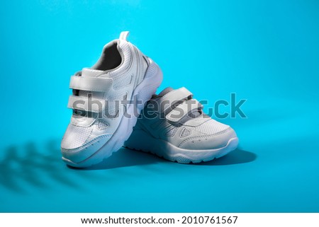 front view of a composition of white children's sneakers on a blue background with shadows from a palm branch.