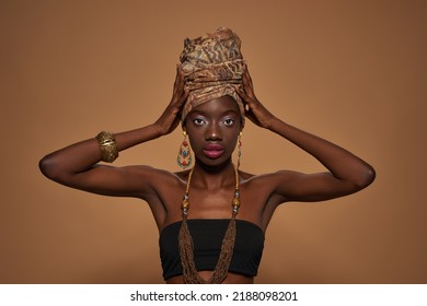Front view of confident elegant black girl wearing traditional african outfit and accessories looking at camera. Beautiful young slim woman. Isolated on orange background. Studio shoot. Copy space - Shutterstock ID 2188098201