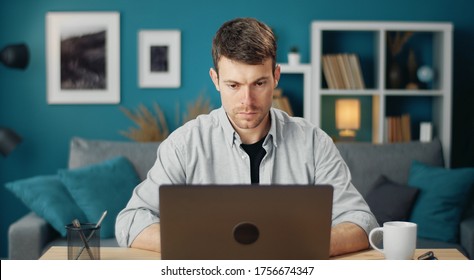 Front view of consumed young man working on laptop computer sitting at desk at home
