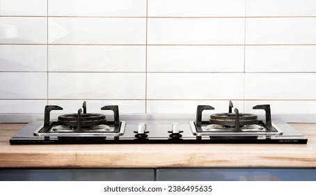Front view of Contemporary tempered glass gas stove hob with Two burners with auto ignition knob on wooden countertop, cast iron pan supports fan hood and oven built in compact