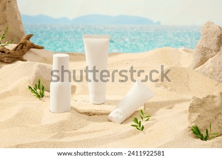 Front view of cosmetic set with white plastic tubes and bottle displayed on sand and blue sea background. Surround is dry twig, grass and blocks of stone. Mockup scene for advertising
