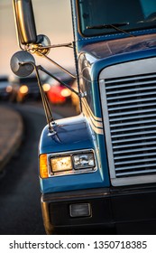 Front View Of Covered With Road Dust Blue Big Rig American Bonnet Classic Semi Truck With Aluminum Grille And Turn On Headlight Driving In Front Of Another Traffic On The Turning Road