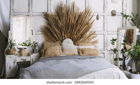 Front View Of Cozy Bedroom With Interior Design In Boho Chic Style, Comfortable Bed, Pillows, Plaid And Green Houseplant Decor Near Mirror On Commode