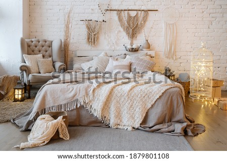 Front view of cozy bedroom with soft plaid and warmth blanket on comfortable bed, pillows, cushions, armchair, home decor and interior design in bohemian style