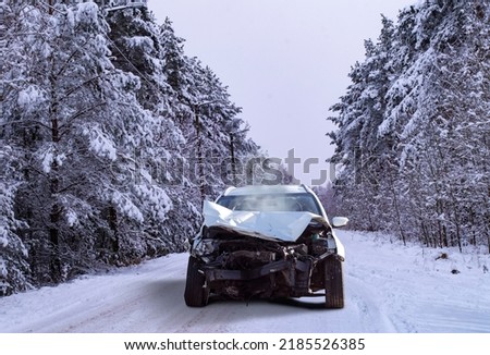 Front view of a crashed car wreck in winter forest background on a snowy slippery road