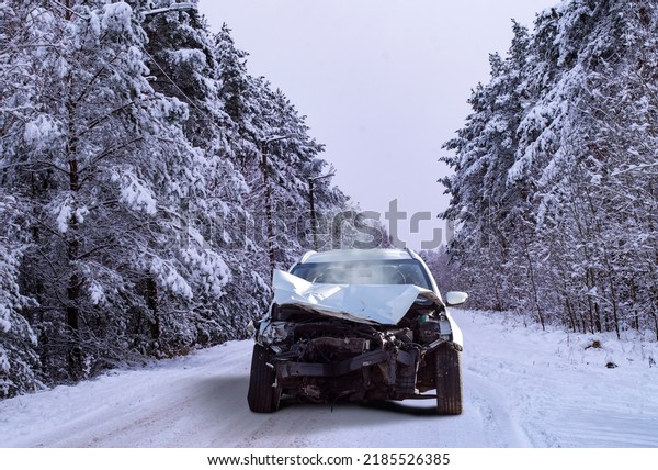 Front view of a crashed car wreck in winter\
forest background on a snowy slippery\
road
