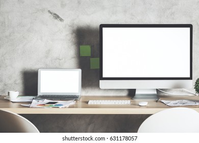 Front View Of Creative Designer Desktop With Large Blank White Computer Screen, Laptop And Supplies. Shadow On Concrete Wall. Mock Up