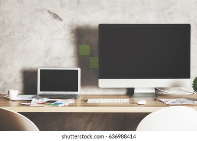 Front View Of Creative Designer Desktop With Large Blank White Computer Screen, Laptop And Supplies. Shadow On Concrete Wall. Mock Up