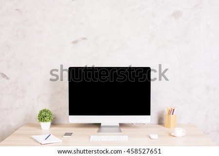 Front view of creative designer desktop with blank computer monitor, coffee cup, smartphone, keyboard, stationery items and plant on concrete wall background. Mock up