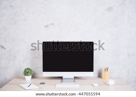 Front view of creative hipster desktop with blank computer screen, coffee cup, smart phone and other items on concrete background. Mock up