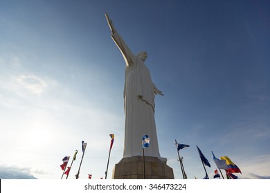 Front view of Cristo del Rey statue of Cali against a blue sky with international flags waving around. Colombia