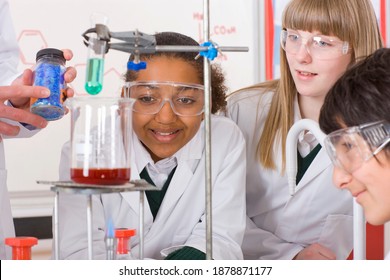 Front view of curious students wearing lab coats and safety goggles closely watching an experiment conducted by the chemistry teacher in a science laboratory - Powered by Shutterstock