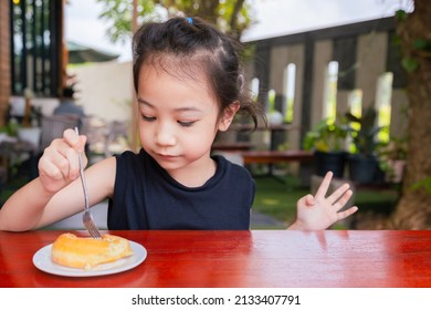 Front View Of Cute 5 Years Old Asian Girl Is Eating Delicious Sweet (donut) Outside The Cafe Shows Concept Of Happy Eating For Kid Or Child With Face Expression Of Enjoyment And Cheerfulness.