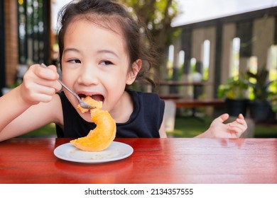 Front View Of Cute 5 Years Old Asian Girl Is Eating Delicious Sweet (donut) Outside The Cafe Shows Concept Of Happy Eating For Kid Or Child With Face Expression Of Enjoyment And Cheerfulness.