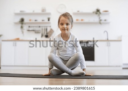 Front view of cute girl practicing yoga, standing in crane exercise, bakasana pose, working out on mat wearing sportswear, indoor full length, in white loft kitchen background.