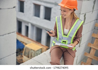 Front view of a cute merry young blonde female worker leaning against the brick wall - Powered by Shutterstock