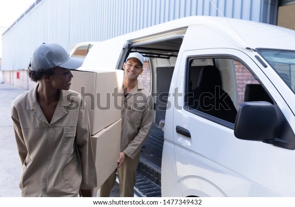 Front view of delivery man and woman carrying\
cardboard boxes near van outside the warehouse. This is a freight\
transportation and distribution warehouse. Industrial and\
industrial workers\
concept