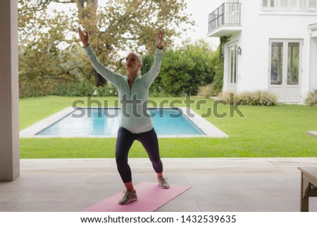 Front view of determined active senior Caucasian woman doing yoga on exercise mat in the porch at home