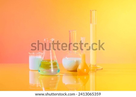Front view of different types of laboratory glassware filled with colorful liquid decorated over gradient yellow and pink background. Laboratory experience and research concept