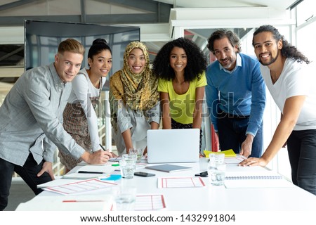 Front view of diverse business people looking at camera while working together at conference room in a modern office