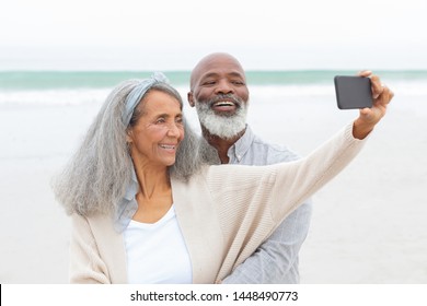 Front view of diverse Couple taking a picture with smartphone at the beach. Authentic Senior Retired Life Concept