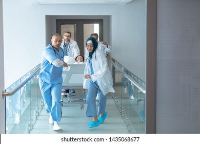 Front View Of Diverse Doctors Pushing Emergency Stretcher Bed In Corridor At Hospital. Asian Female Patient Is Lying In Stretcher Bed.