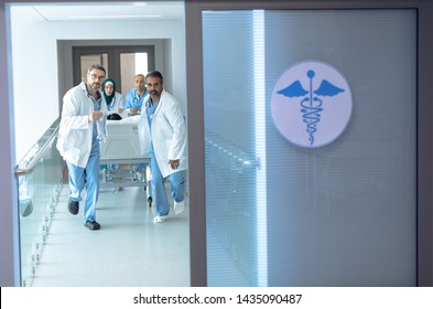 Front View Of Diverse Doctors Pushing Emergency Stretcher Bed In Corridor At Hospital.