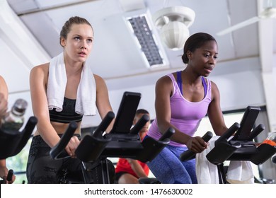 Front view of diverse fit women exercising on exercise bike in fitness center. Bright modern gym with fit healthy people working out and training at spin class - Powered by Shutterstock