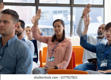 Front View Of A Diverse Group Of Business Creatives Sitting In The Audience At A Business Conference, All Raising Their Hands To Ask Questions