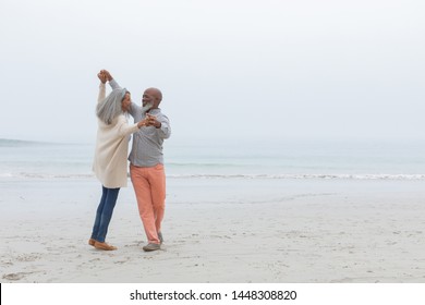 Front view of diverse happy senior couple smiling and dancing on the beach on cloudy day. Authentic Senior Retired Life Concept - Powered by Shutterstock