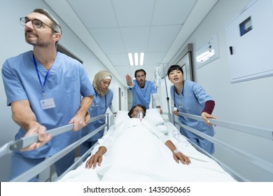 Front View Of Diverse Medical Team Pushing Emergency Stretcher Bed In Corridor At Hospital. Mixed-race Female Patient