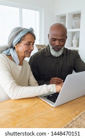 Front View Of Diverse Senior Couple Using Laptop On Table Inside A Room In Beach House. Authentic Senior Retired Life Concept