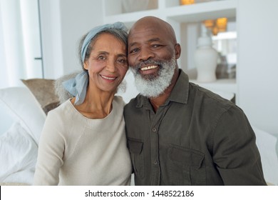 Front view of diverse senior couple smiling while sitting on a couch inside a room in beach house. Authentic Senior Retired Life Concept - Powered by Shutterstock